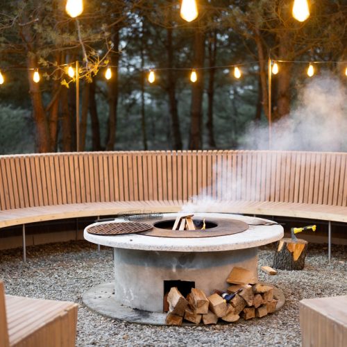 Beautiful lounge area with fireplace, round bench and illuminated garlands in forest at dusk